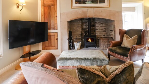 A cozy living room with a fireplace, leather armchairs, a flat-screen TV, and a comfortable ottoman. - Squint Cottage (Skipton)