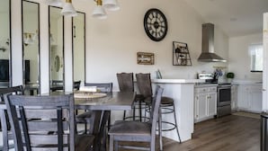 A modern kitchen with white cabinets, a central island, and a dining area with dark wooden chairs. - The Hillview Hangout (Grand Junction)
