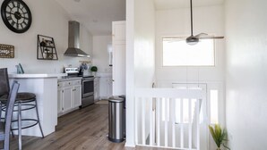 A modern kitchen with white cabinetry, a stainless steel range hood, and a bar area with stools. - The Hillview Hangout (Grand Junction)