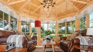 A cozy room with a wooden ceiling, leather sofas, a coffee table, and a bookshelf.
