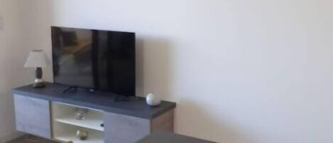 A modern living room with a flat-screen TV on a grey cabinet, a dining table with chairs, and a painting of red flowers on the wall.