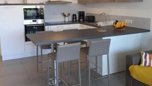 Eine moderne Küche mit einer zentralen Kochinsel, Barhocker, einer Kaffeemaschine und einer Obstschale.