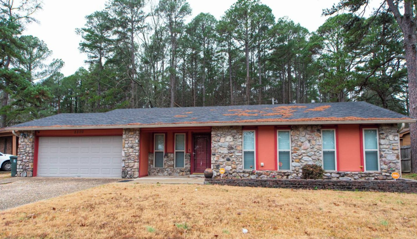 A single-story house with a stone facade, a red front door, and a garage.