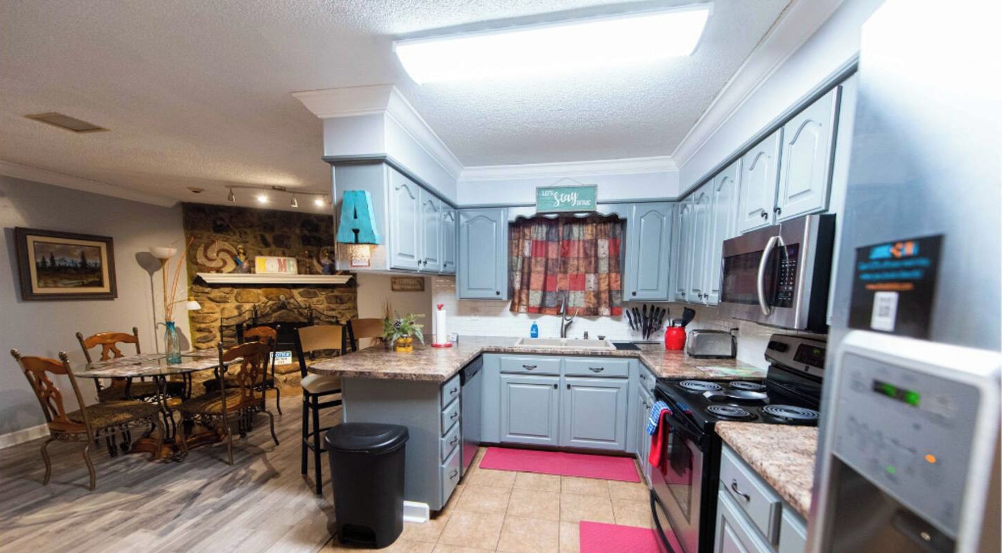 Een moderne keuken met grijze kastjes, een accentmuur van steen, een eethoek met een houten tafel en stoelen, en een keukeneiland.