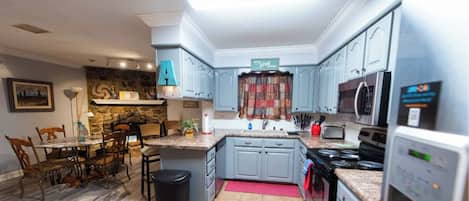 Een moderne keuken met grijze kastjes, een accentmuur van steen, een eethoek met een houten tafel en stoelen, en een keukeneiland.