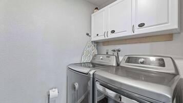 A laundry area with two stacked washers and dryers, white cabinets above, and a patterned towel hanging on the wall.