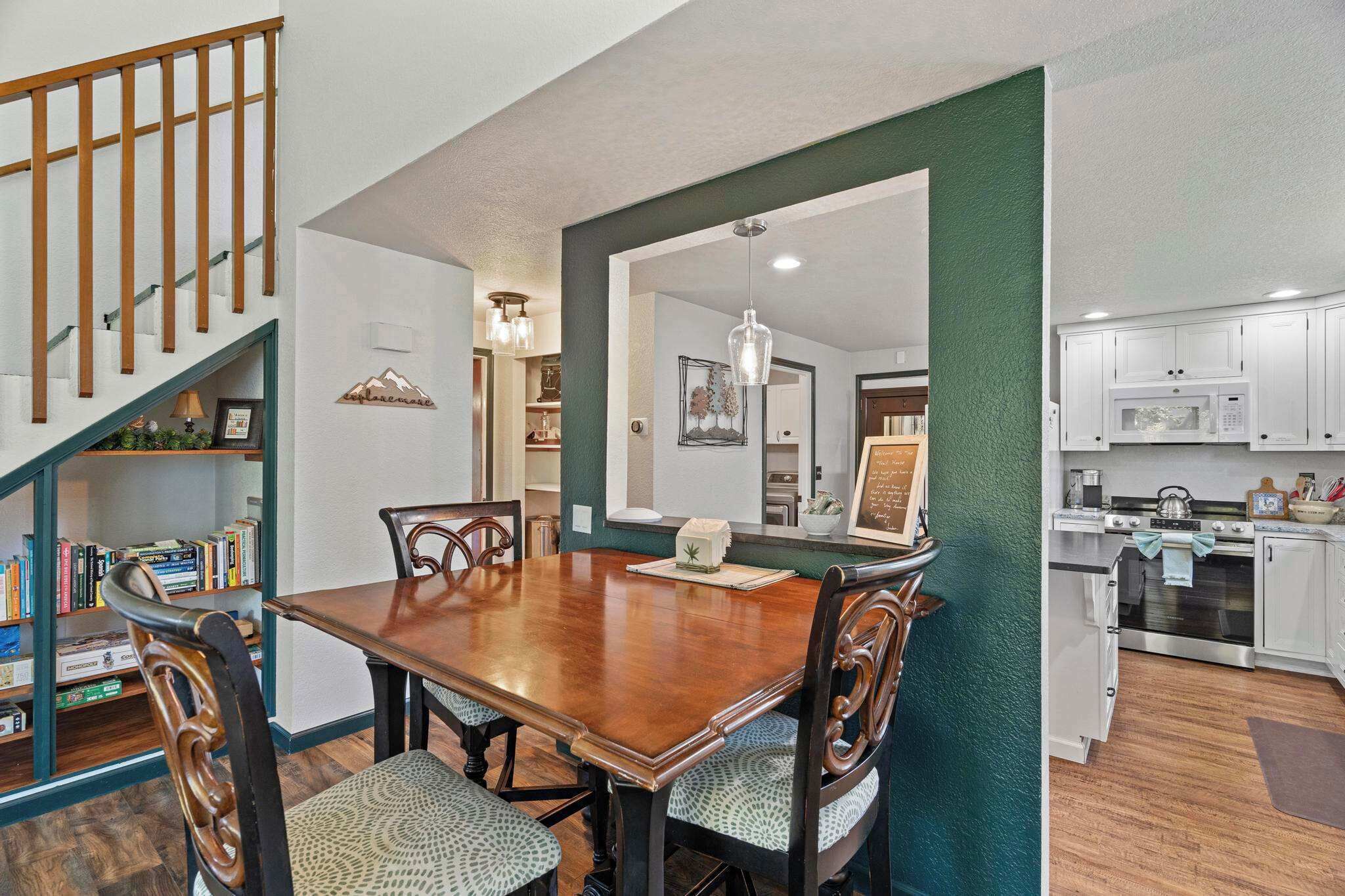 A dining area with a wooden table and chairs, a bookshelf, and a staircase.