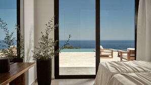 Ein Schlafzimmer mit einer großen Schiebeglastür, die auf einen Balkon mit Meerblick führt.