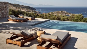 Ein Poolbereich mit Liegestühlen und Blick auf Meer und Berge.