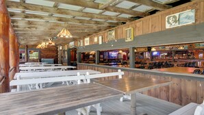 Un interior rústico con mesas y bancos de madera, una zona de bar, y diversos carteles y adornos.