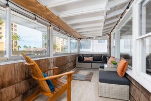 Relax in this serene sunroom with a view of the surrounding buildings and palm trees, featuring a comfortable sofa and a cozy rocking chair.