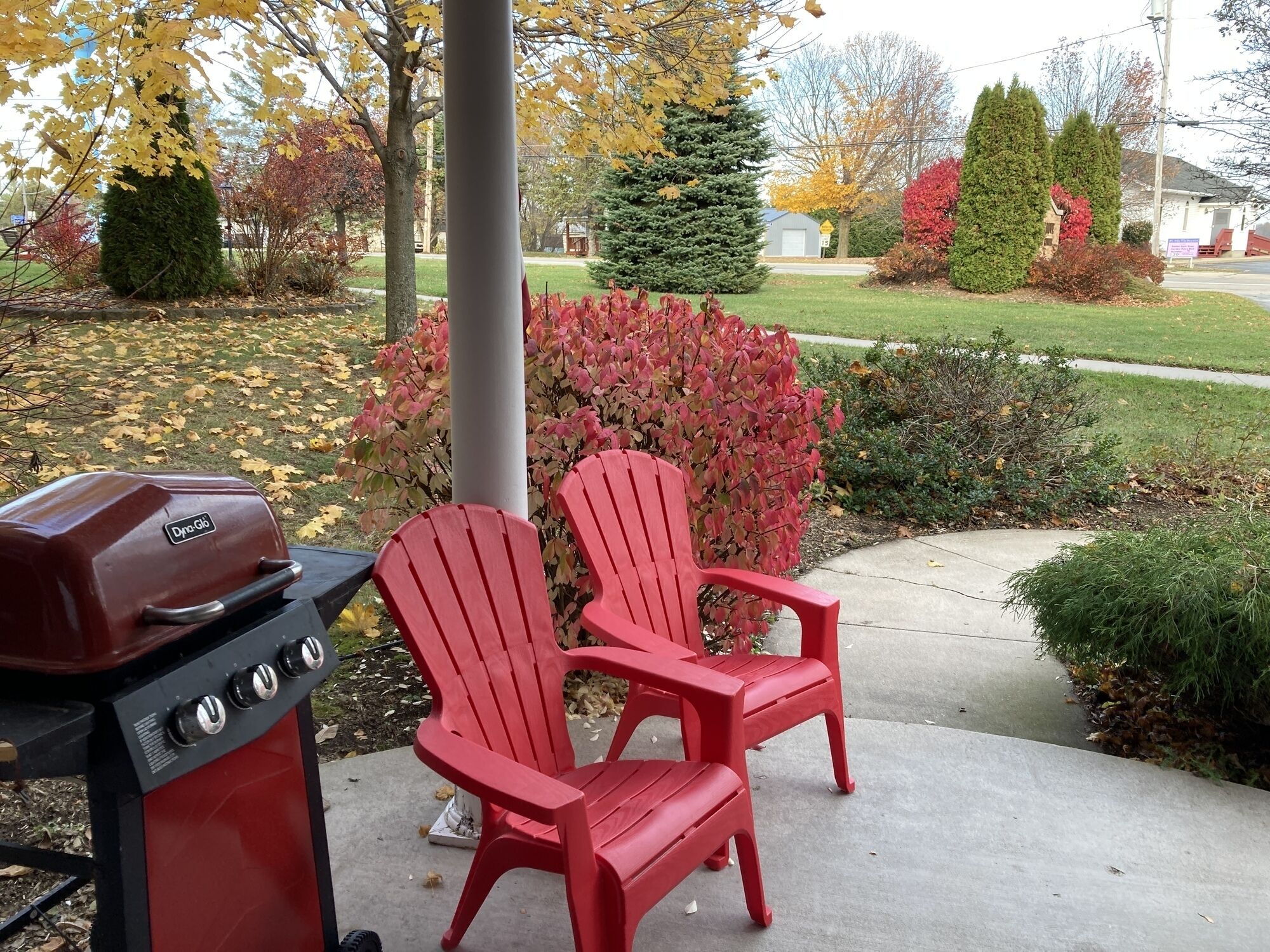 Un barbecue et deux chaises Adirondack rouges dans un jardin aux couleurs automnales.