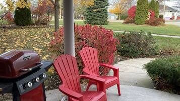 Un barbecue et deux chaises Adirondack rouges dans un jardin aux couleurs automnales.