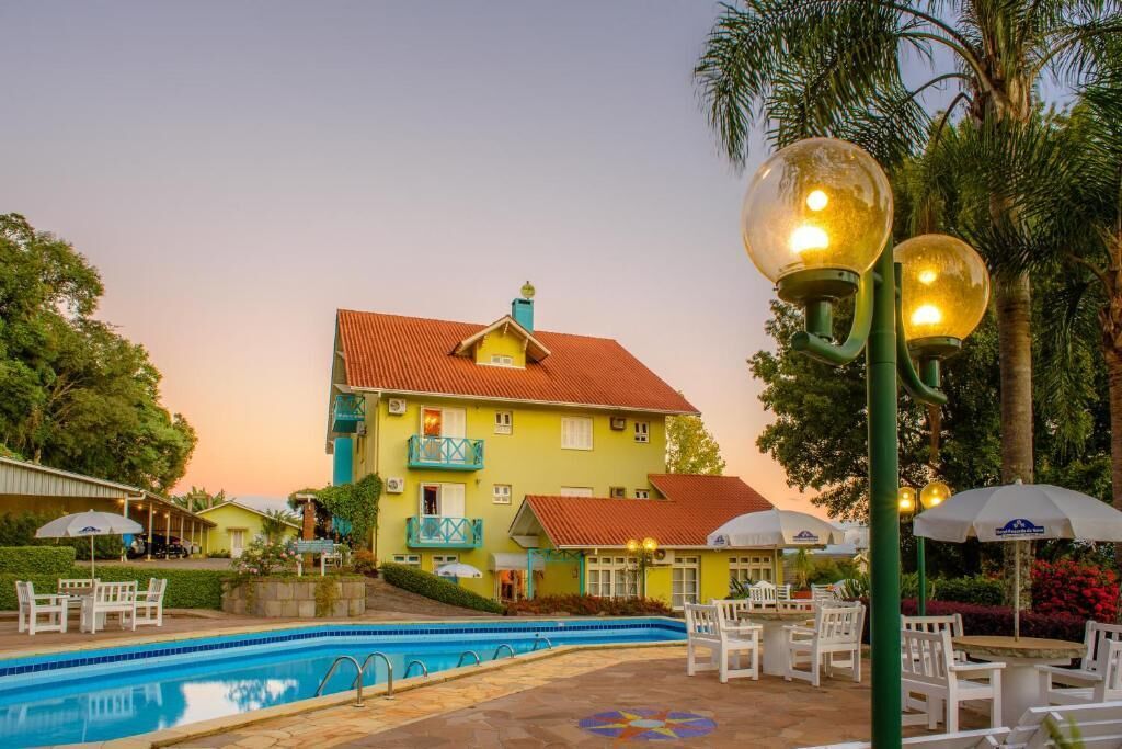 A hotel with a swimming pool, outdoor seating, and a large building with a red roof.