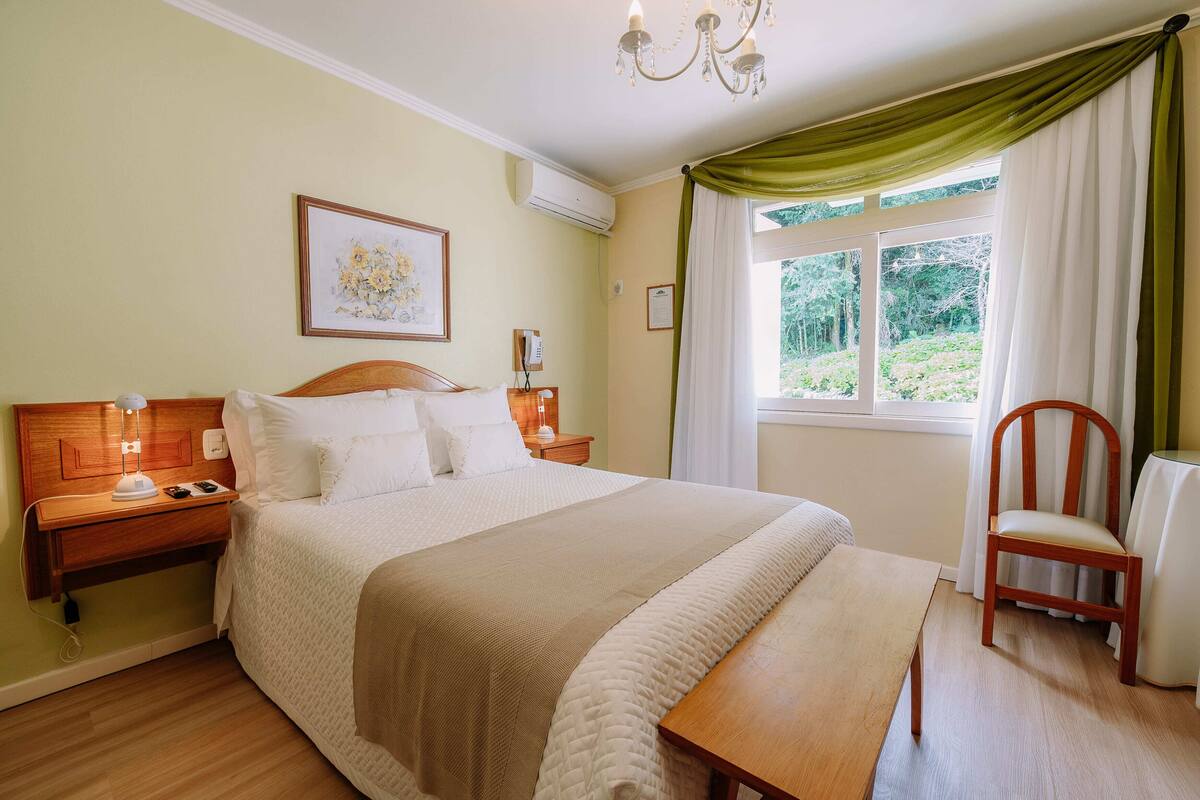 A neatly arranged bedroom with a bed, bedside tables, a chair, and a window with curtains.