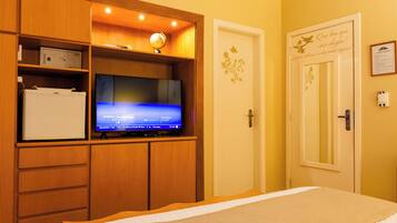 A hotel room with a bed, a television on a wooden cabinet, a door with a decorative sticker, and a wall-mounted light fixture.
