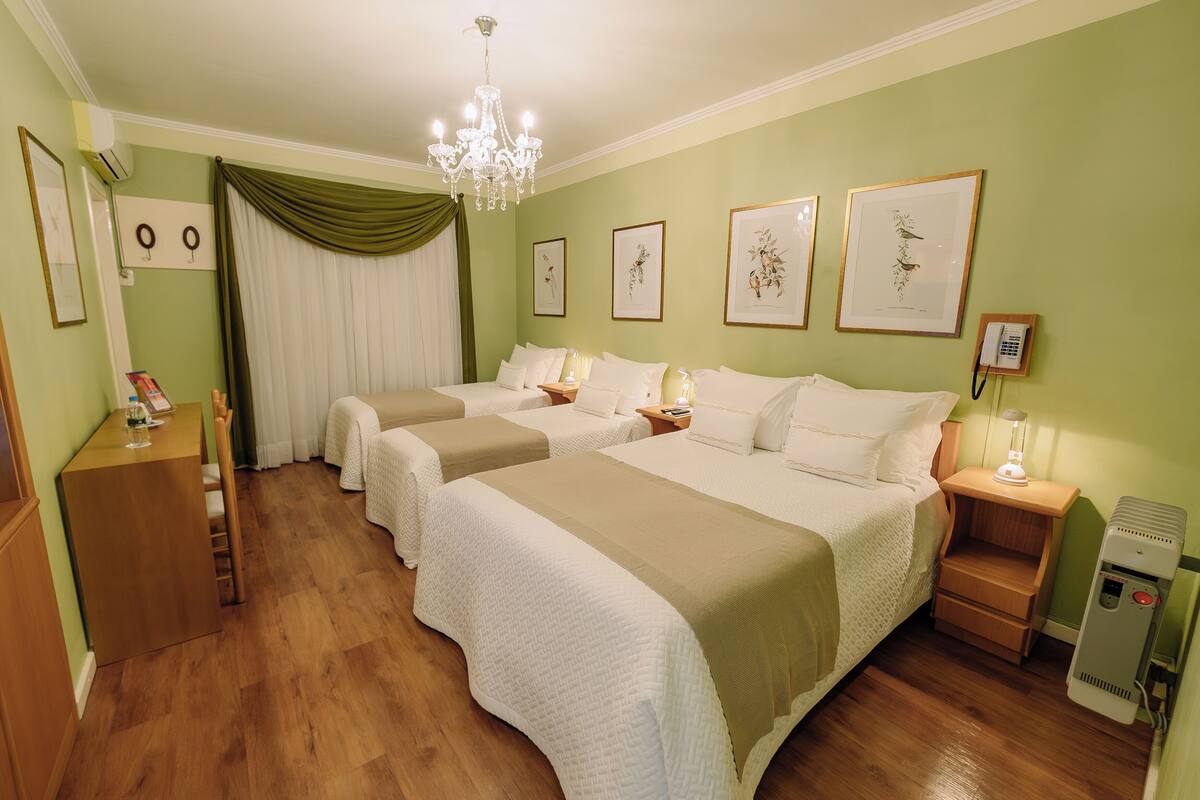 A hotel room with four beds, a chandelier, framed botanical prints, a telephone, and a heater.