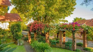 A garden pathway leading to a brick archway with benches, surrounded by lush greenery and flowering plants. - HOTEL POUSADA DA NEVE (Nova Petropolis)