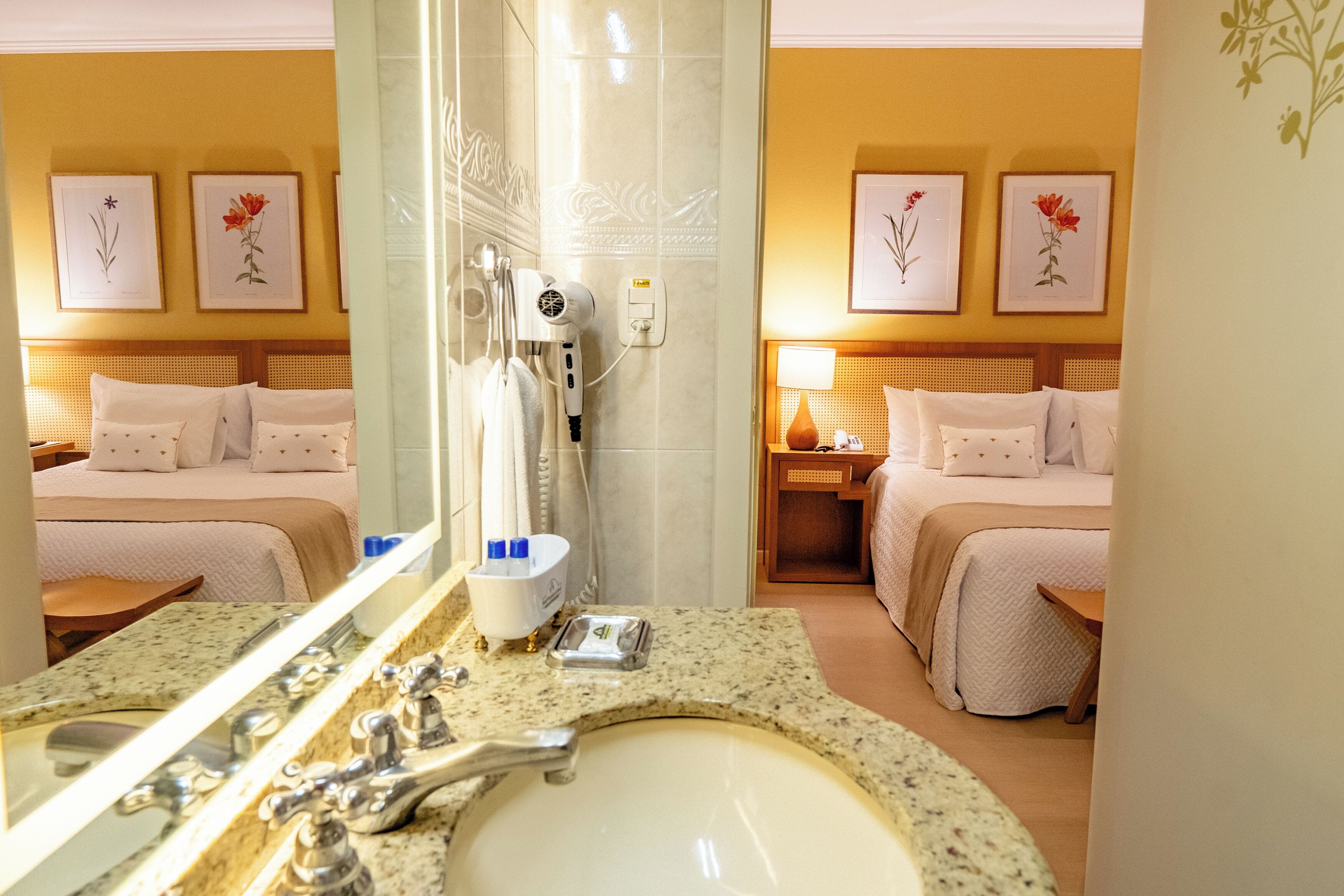 Un baño de hotel con un lavamanos, espejo y dos camas con cabeceros.