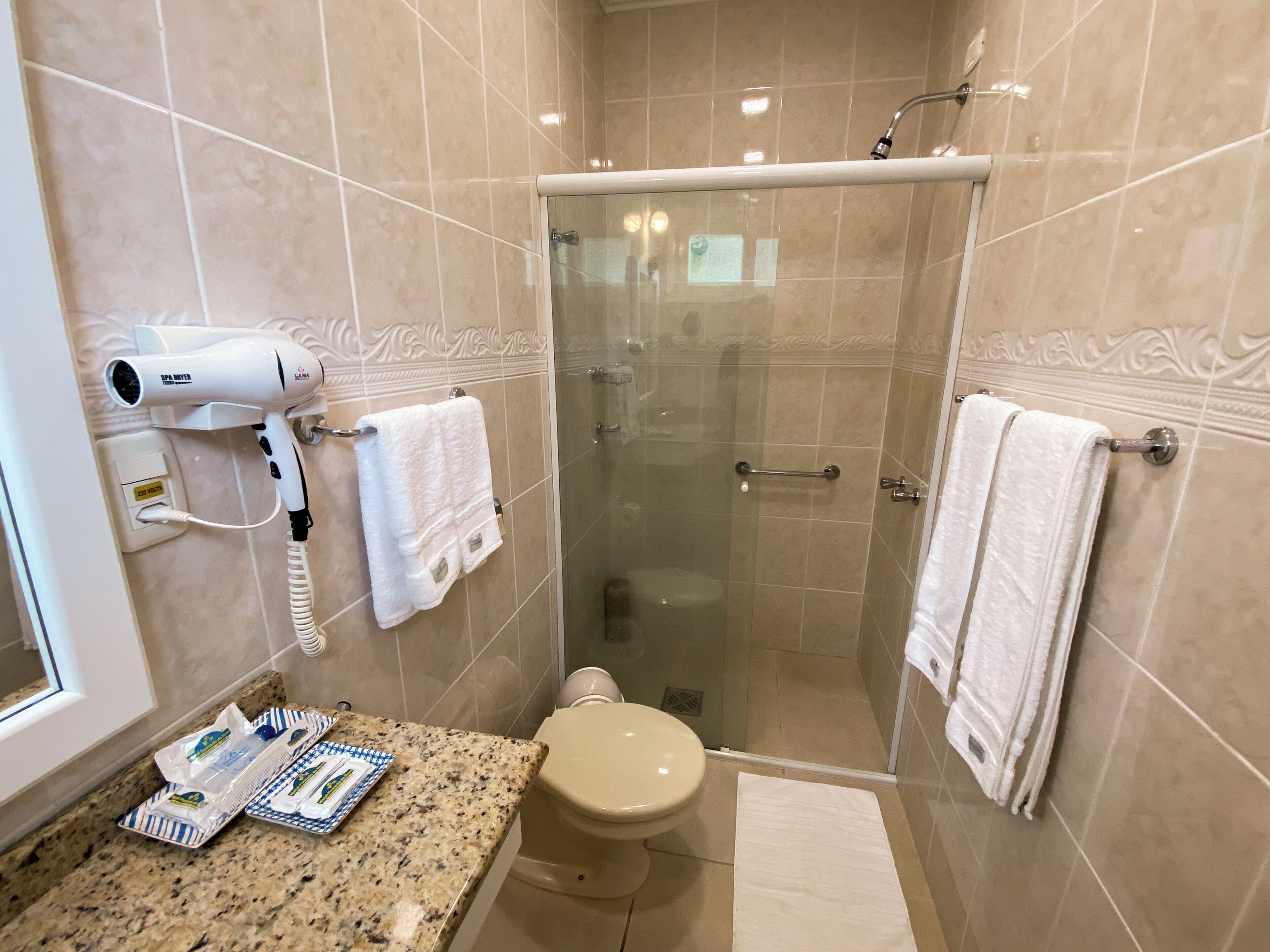 A bathroom with a hairdryer, two towels, a toilet, and a shower area.