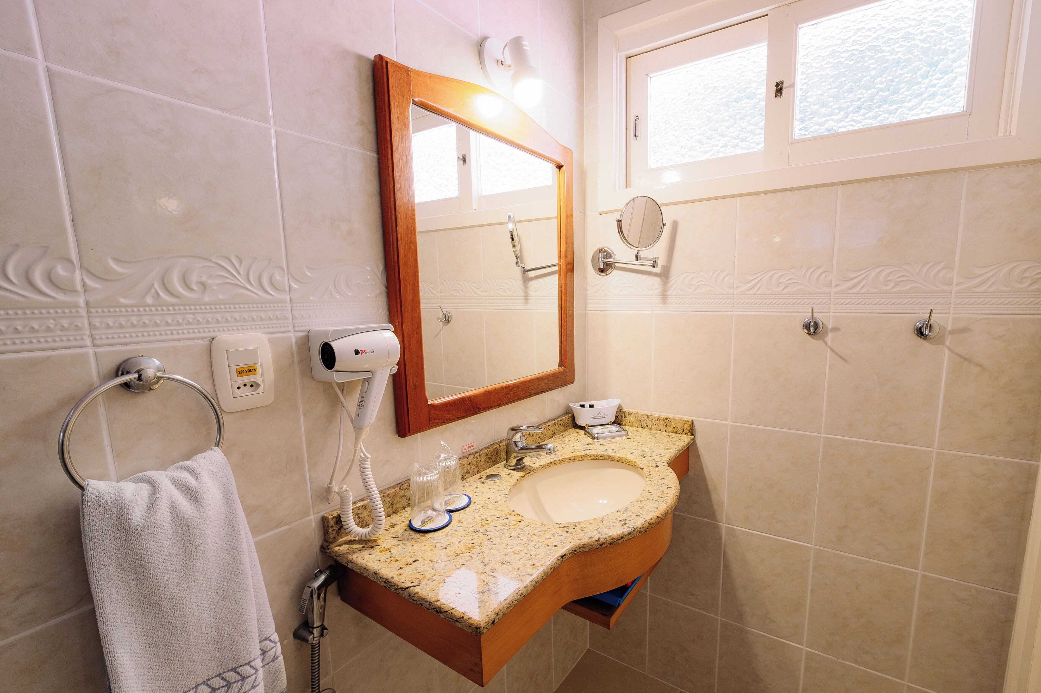 A bathroom with a sink, mirror, towel ring, and a window.