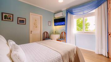 A bedroom with a bed, a TV, a window with curtains, and a door.