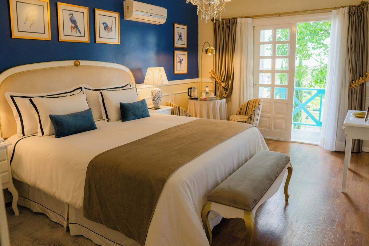 A bedroom with a large bed, bedside tables, a lamp, a chair, a small table, and a door leading to an outdoor area.