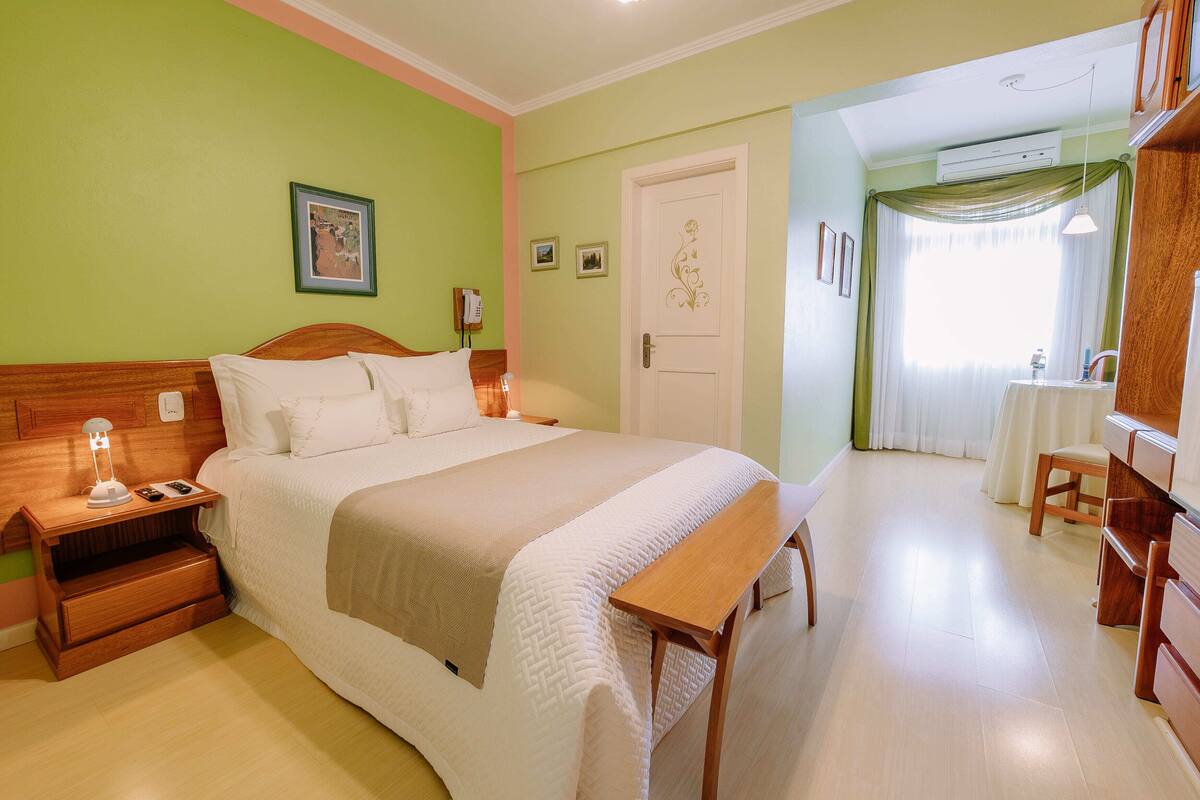 A neatly arranged bedroom with a bed, bedside table, lamp, and a small table with a chair.