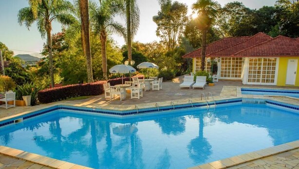 A swimming pool with a tiled edge, surrounded by stone tiles and white lounge chairs. - HOTEL POUSADA DA NEVE (Nova Petropolis)