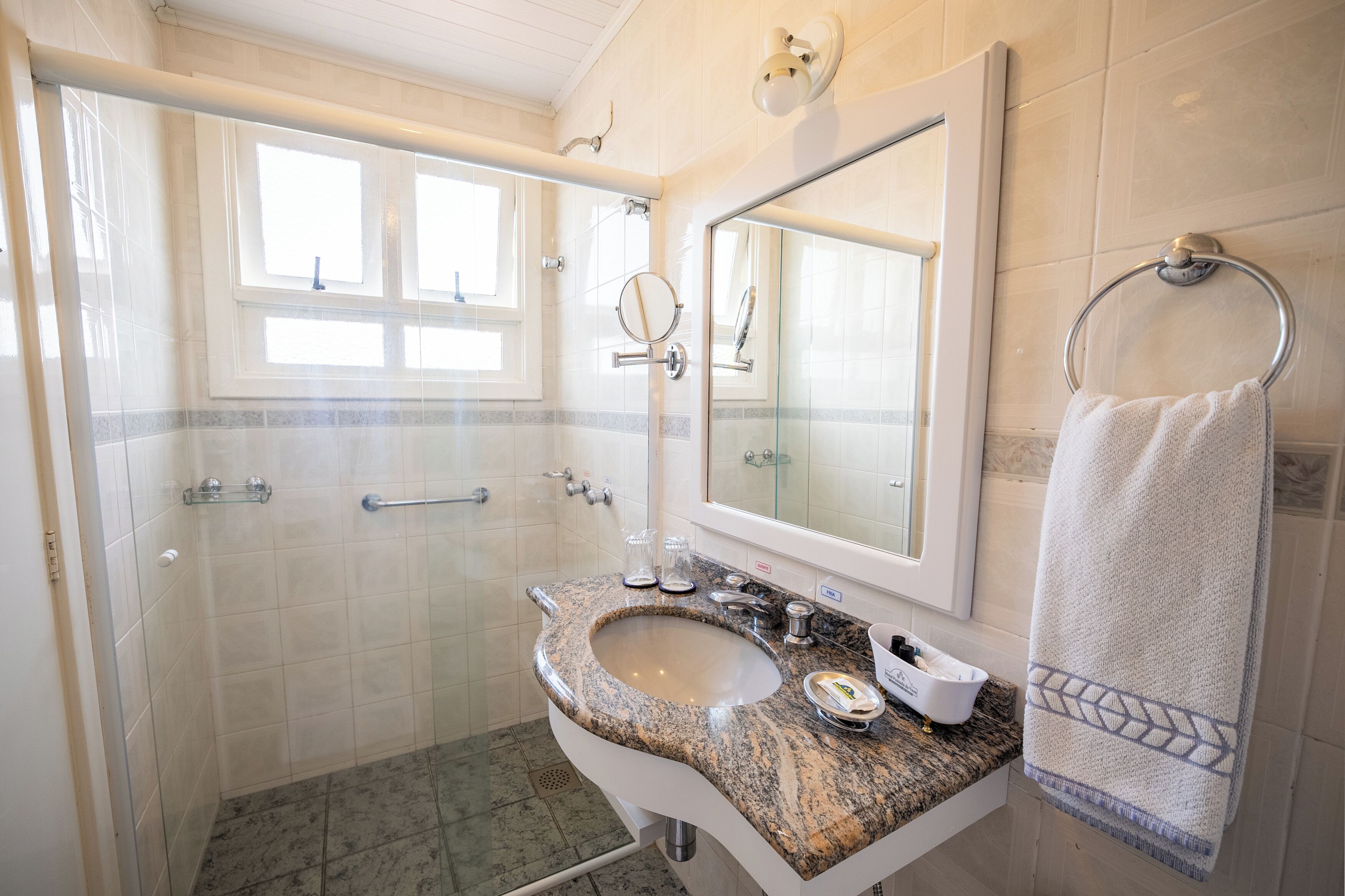 Un baño con lavamanos de granito, un espejo grande, toallero y zona de ducha.