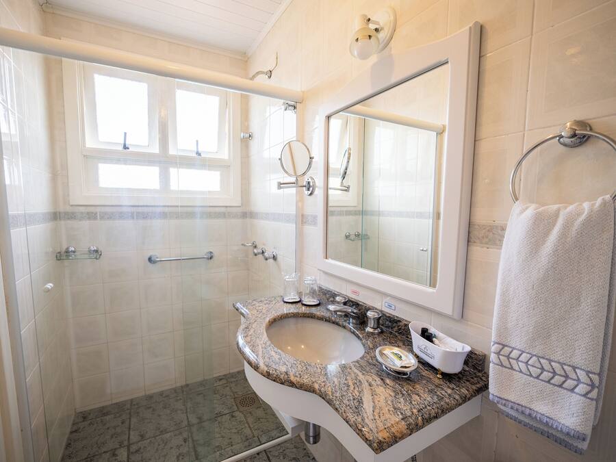 Un baño con lavamanos de granito, un espejo grande, toallero y zona de ducha.