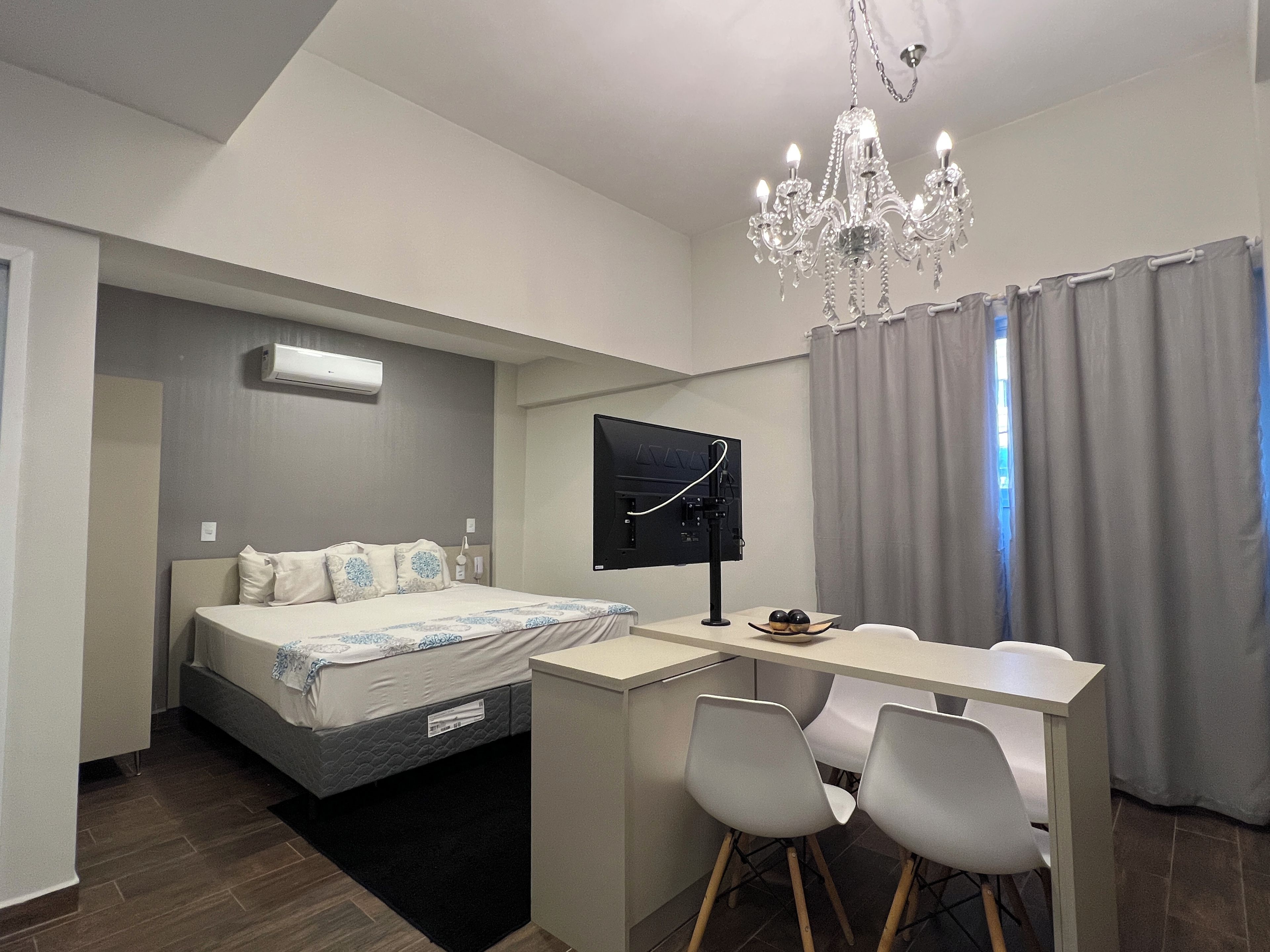 Ein modernes Hotelzimmer mit Bett, Schreibtisch, zwei Stühlen, Fernseher und einer Deckenleuchte.