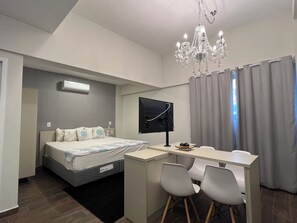 A modern hotel room with a bed, desk, two chairs, a TV, and a chandelier. - Esuites Sorocaba (Sorocaba)
