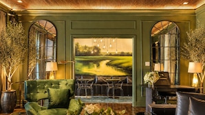 A green-themed lobby with a large painting of a landscape, leather seating, and tall lamps.