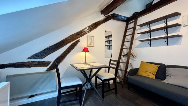 A cozy attic room with a dining table, chairs, a sofa, and a ladder. - Charming, neat and bright studio, in a lively area, 15 minutes from the Louvre (Paris)
