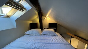 A bedroom with a skylight, a bed with white bedding, two bedside tables with lamps, and a wooden headboard. - Charming, neat and bright studio, in a lively area, 15 minutes from the Louvre (Paris)