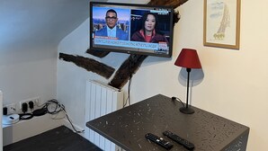 A room with a TV mounted on the wall displaying a news channel, a framed picture of the Eiffel Tower, and a table with two remotes. - Charming, neat and bright studio, in a lively area, 15 minutes from the Louvre (Paris)
