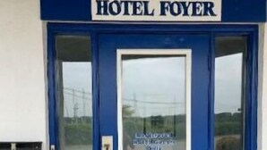 Une porte bleue avec une enseigne indiquant « HÔTEL FOYER » et une fenêtre donnant sur un paysage.