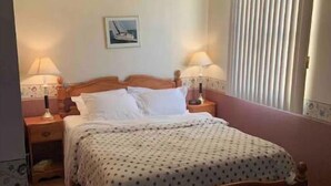 Une chambre à coucher avec un lit en bois, deux tables de chevet avec des lampes, une fenêtre avec des stores et un tableau encadré au mur.