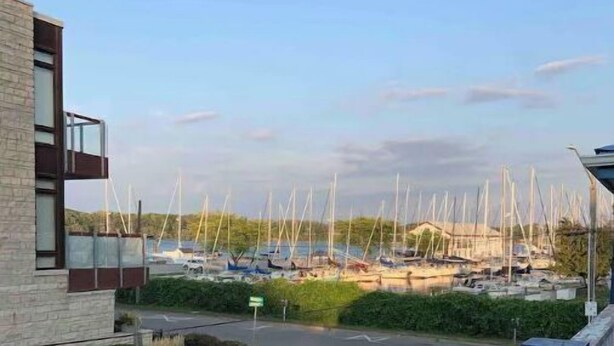 Un port de plaisance où sont amarrés de nombreux voiliers, un espace de stationnement et un bâtiment à la façade en pierre.
