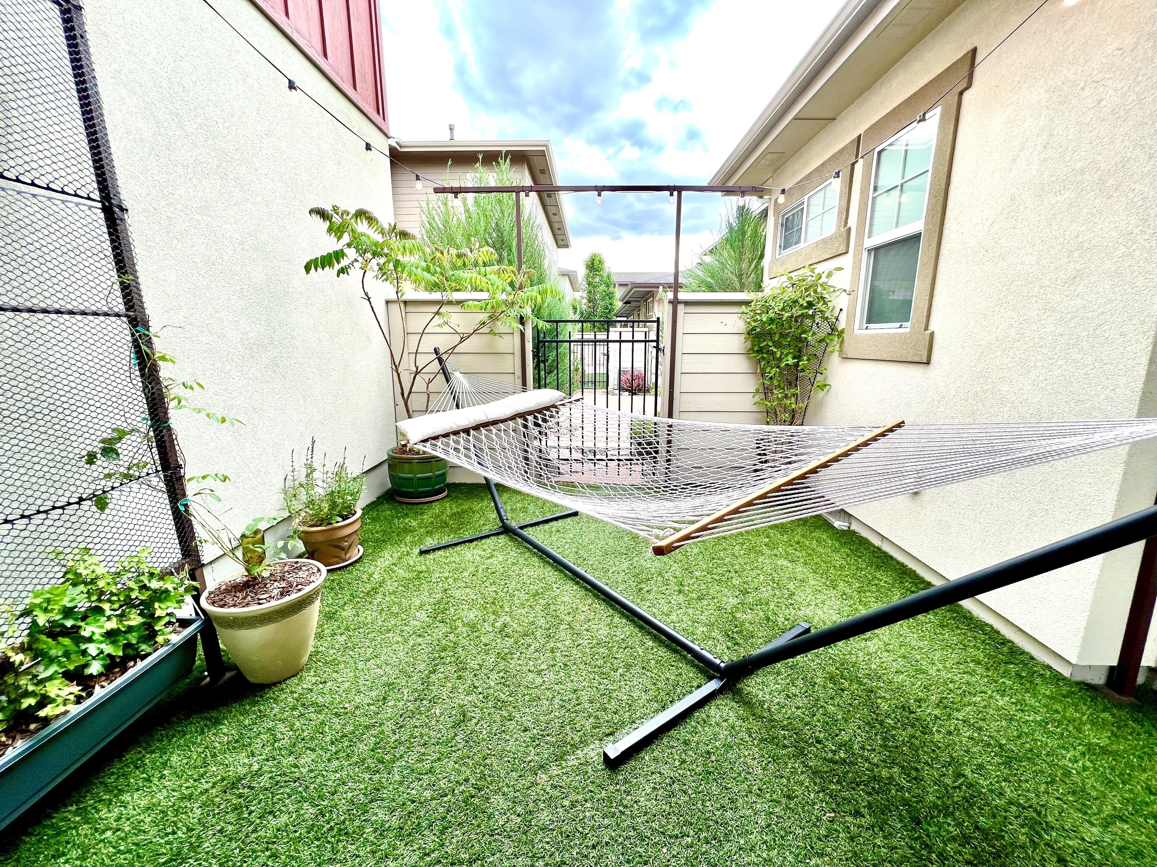 A small, enclosed outdoor space with artificial grass, a hammock, and potted plants.