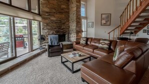 A living room with a stone fireplace, leather sofas, a coffee table, and a staircase. - Powder Run by Park City Vacations (Park City)