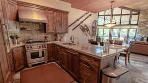 A modern kitchen with wooden cabinets, a stainless steel range, and a large island with a sink. - Powder Run by Park City Vacations (Park City)