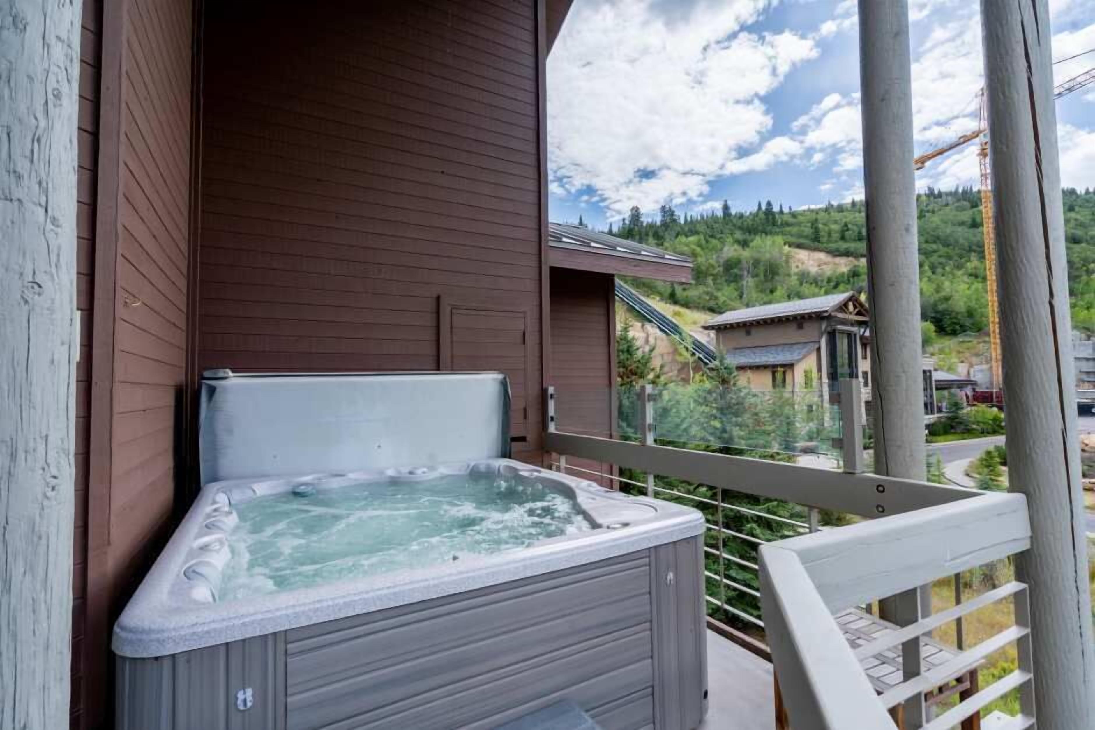 A hot tub on a balcony with a view of a residential area and a hill.
