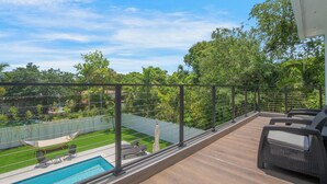 A balcony with a pool, outdoor furniture, and a view of a lush garden. - Luxury 4BR Retreat w/ Heated Pool + Free Car Rental – Near Miami & Beaches (Biscayne Park)