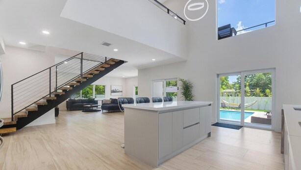 A spacious living area with a central island, a staircase, and a view of the outdoors. - Luxury 4BR Retreat w/ Heated Pool + Free Car Rental – Near Miami & Beaches (Biscayne Park)