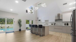 A modern kitchen with a central island, bar stools, and a view of a swimming pool. - Luxury 4BR Retreat w/ Heated Pool + Free Car Rental – Near Miami & Beaches (Biscayne Park)