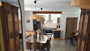 Un comedor espacioso con una mesa grande y sillas, armarios de madera y una cocina al fondo.