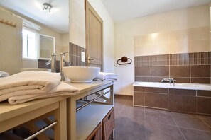 A modern bathroom with a large bathtub, a sink with a bowl, and a mirror.