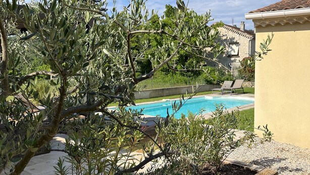 Zona de piscina exterior con pared de piedra, terraza de madera y olivos.